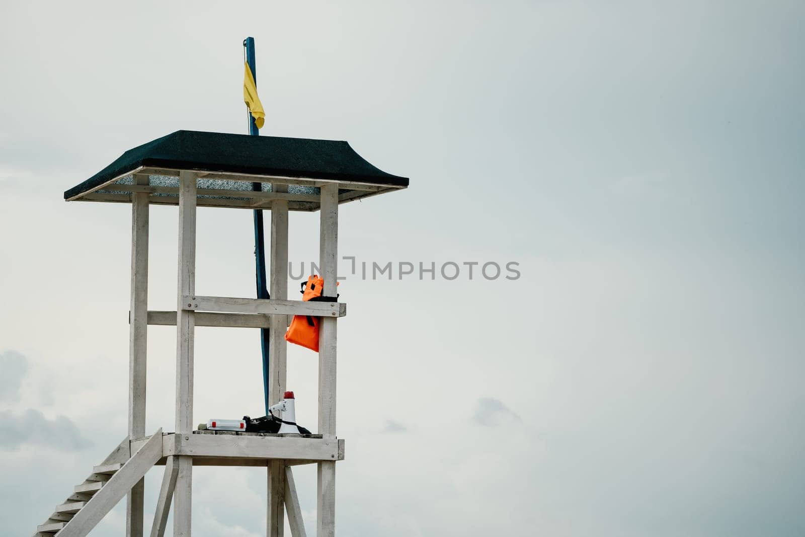 Empty white lifeguard tower with a yellow flag on the beach in windy weather. Beach lifeguard tower with yellow flag indicator. Nobody. Holiday recreation concept