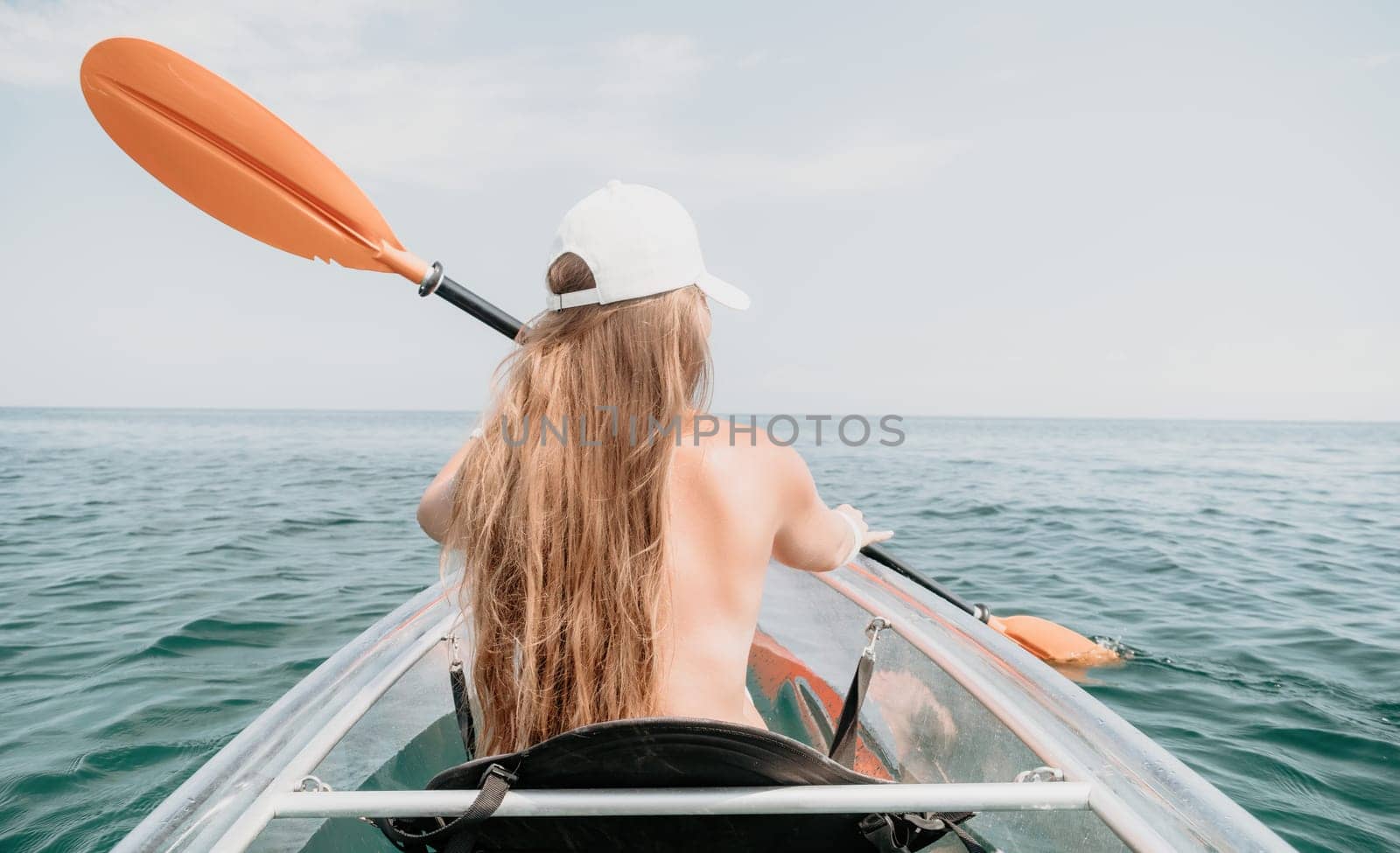 Woman in kayak back view. Happy young woman with long hair floating in transparent kayak on the crystal clear sea. Summer holiday vacation and cheerful female people having fun on the boat.