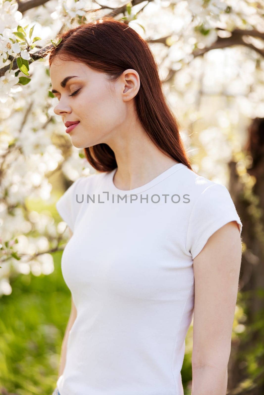 portrait of a lovely, beautiful woman against the backdrop of a flowering tree in a white T-shirt by Vichizh