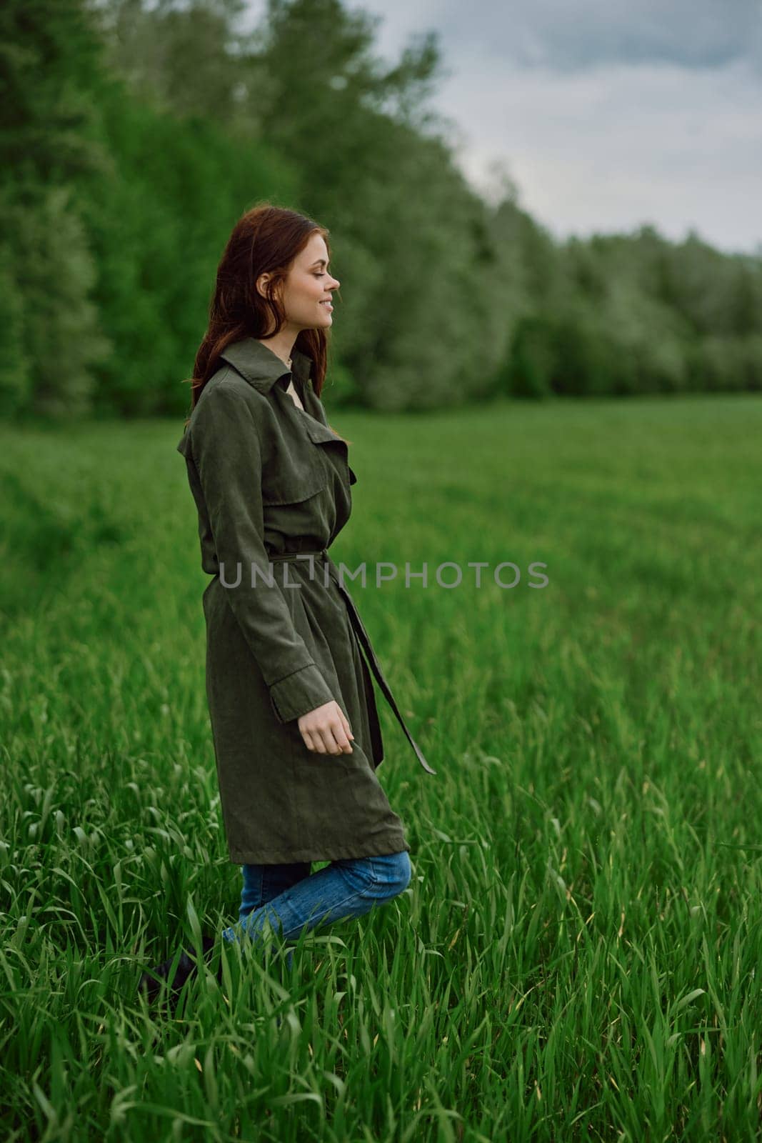 a woman in a long raincoat stands in tall green grass in a field in rainy weather in spring. High quality photo