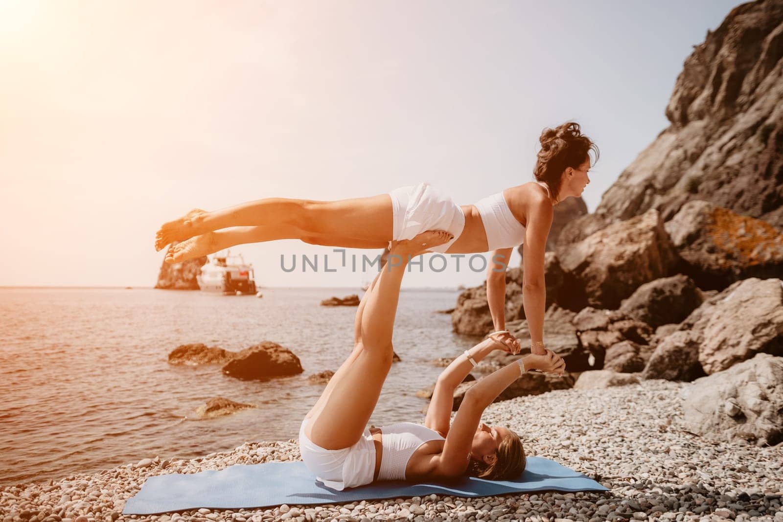 Woman sea yoga. Two Happy women meditating in yoga pose on the beach, ocean and rock mountains. Motivation and inspirational fit and exercising. Healthy lifestyle outdoors in nature, fitness concept. by panophotograph