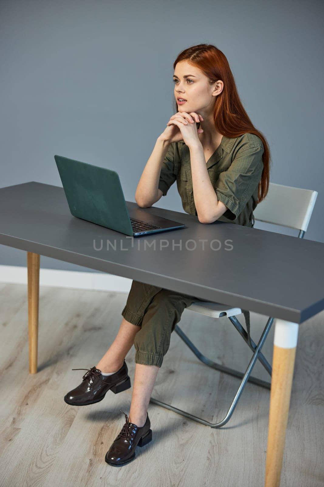 photo of a woman sitting at a table with a laptop in the office against the background of a blue wall. High quality photo