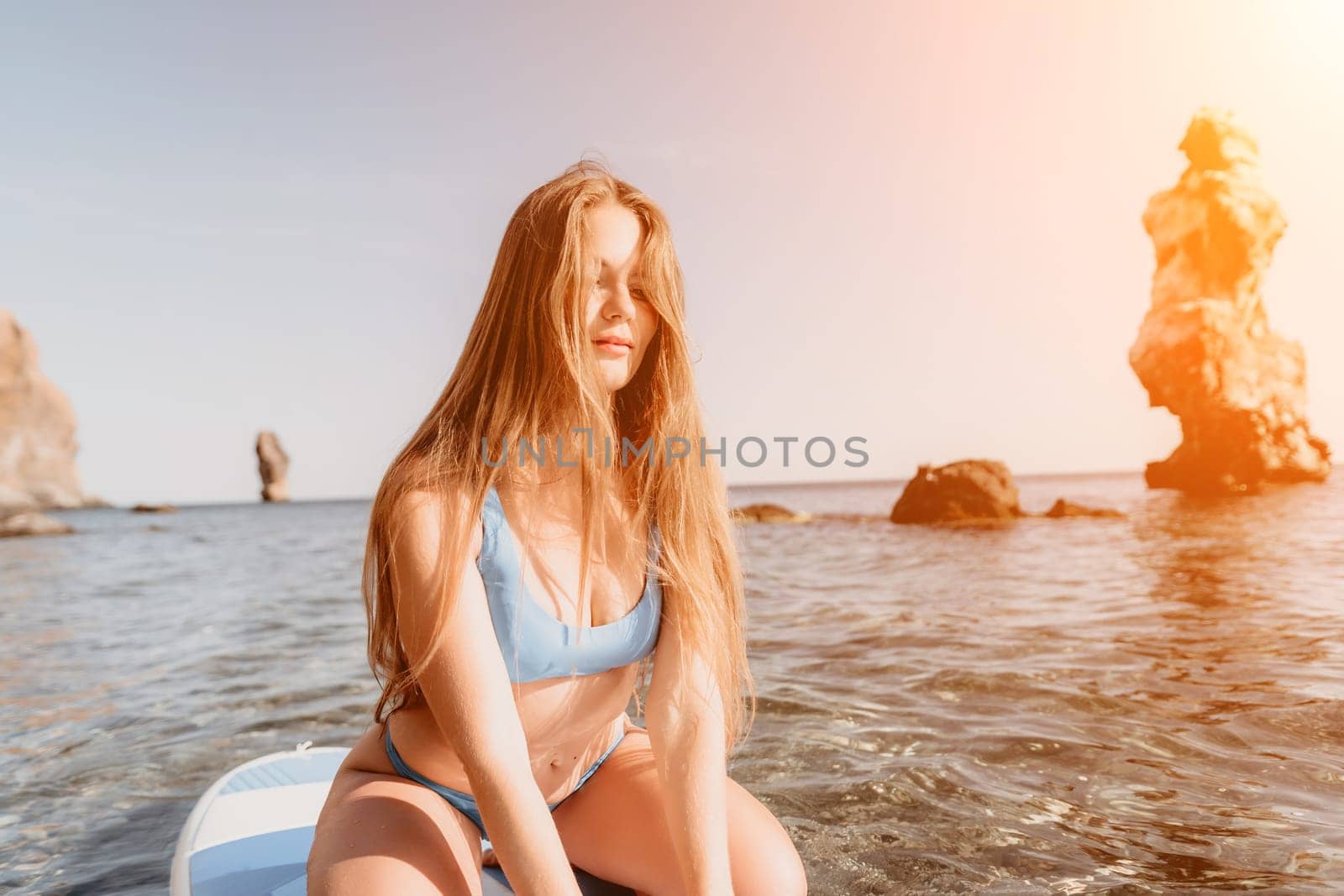 Close up shot of happy young caucasian woman looking at camera and smiling. Cute woman portrait in bikini posing on a volcanic rock high above the sea