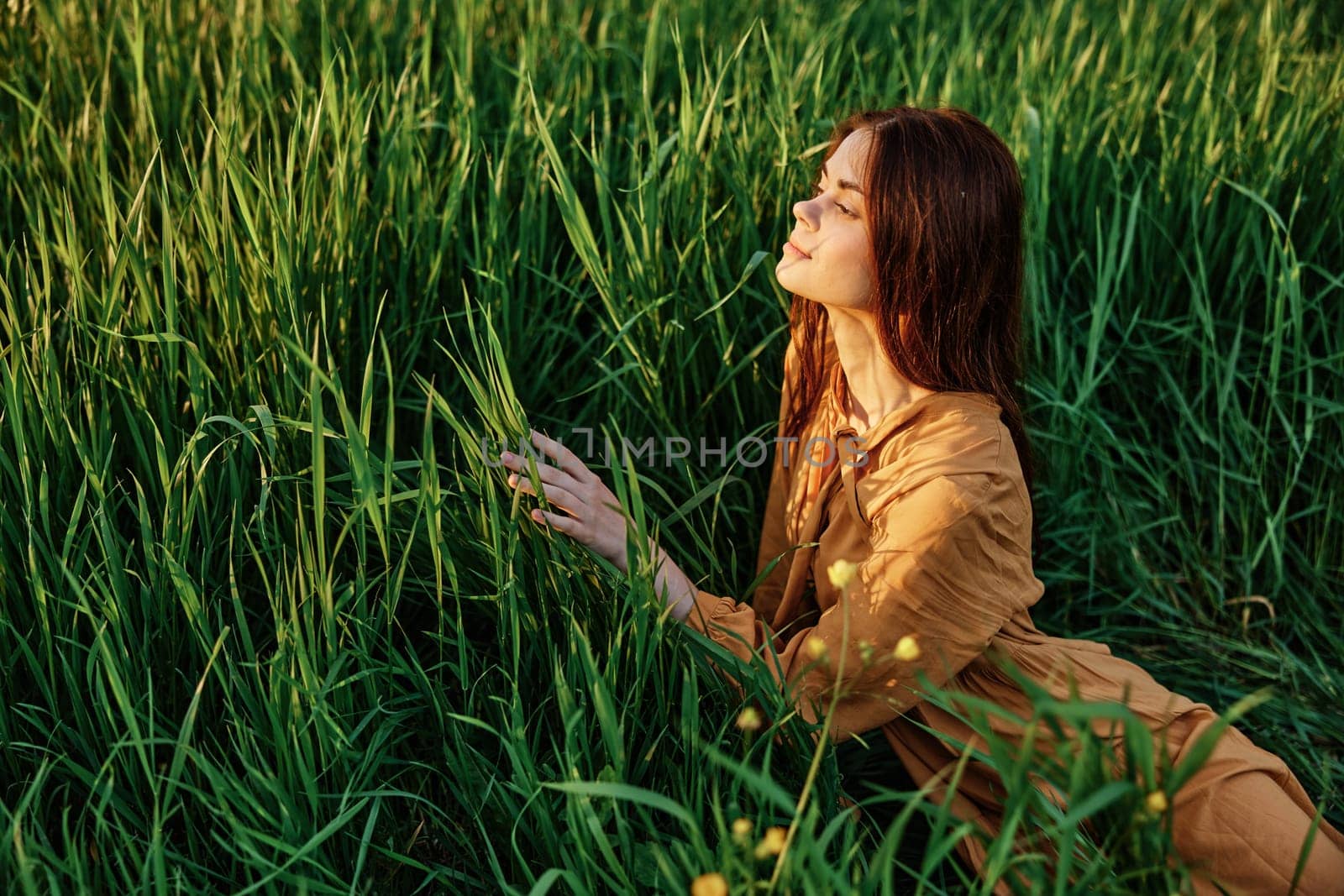 a close horizontal photo of a pleasant woman in a long orange dress resting lying in the tall grass smiling with her eyes closed. Street photography, the theme of privacy with nature. High quality photo