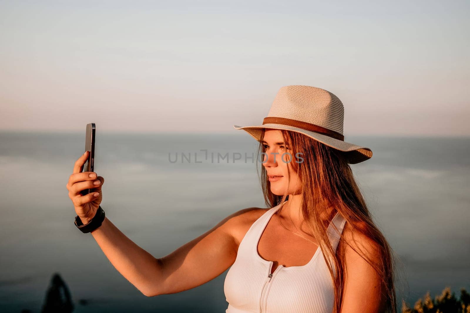 Woman travel sea. Happy tourist in hat enjoy taking picture outdoors for memories. Woman traveler posing on the beach at sea surrounded by volcanic mountains, sharing travel adventure journey. by panophotograph
