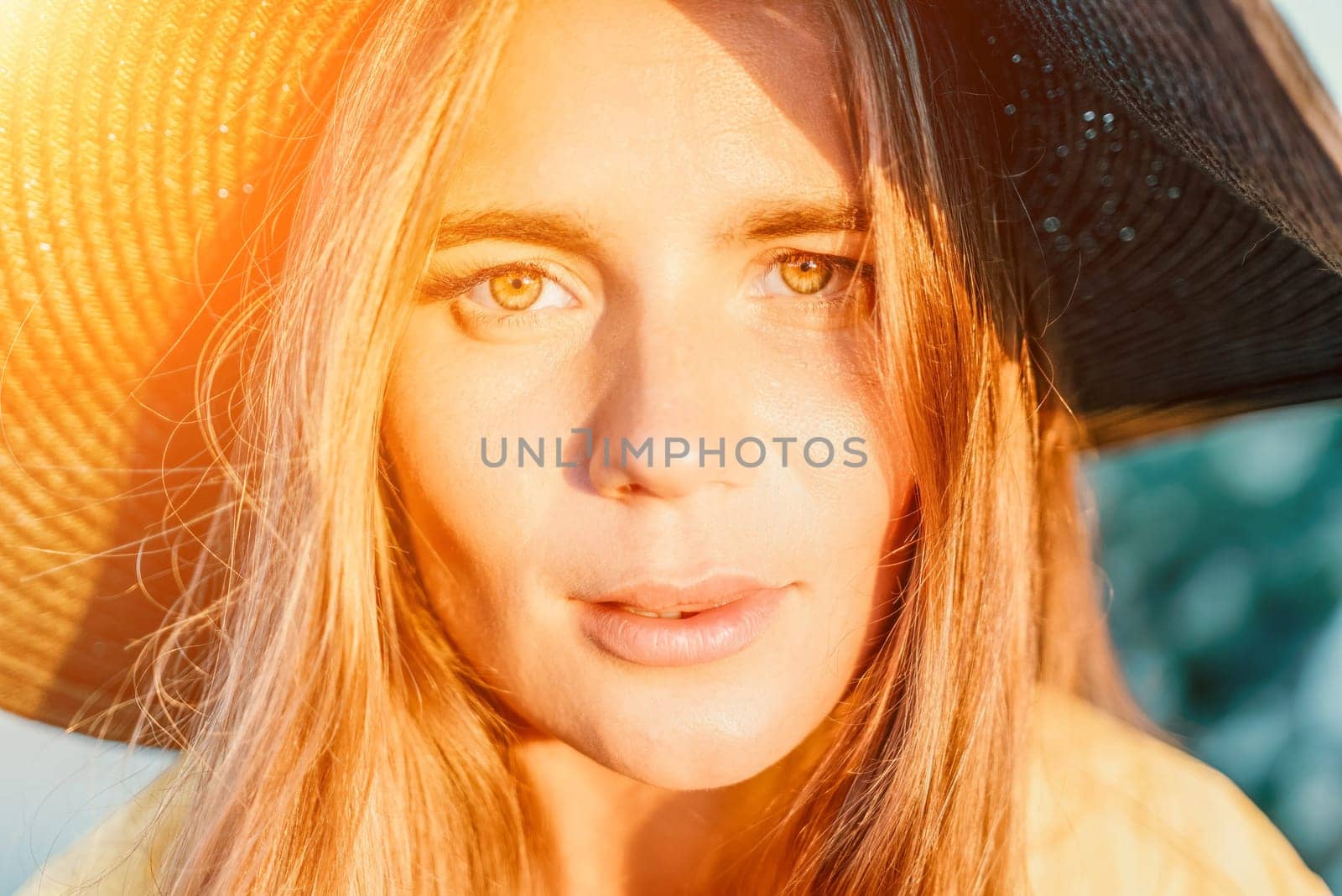 Portrait of happy young woman wearing summer black hat with large brim at beach on sunset. Closeup face of attractive girl with black straw hat. Happy young woman smiling and looking at camera at sea