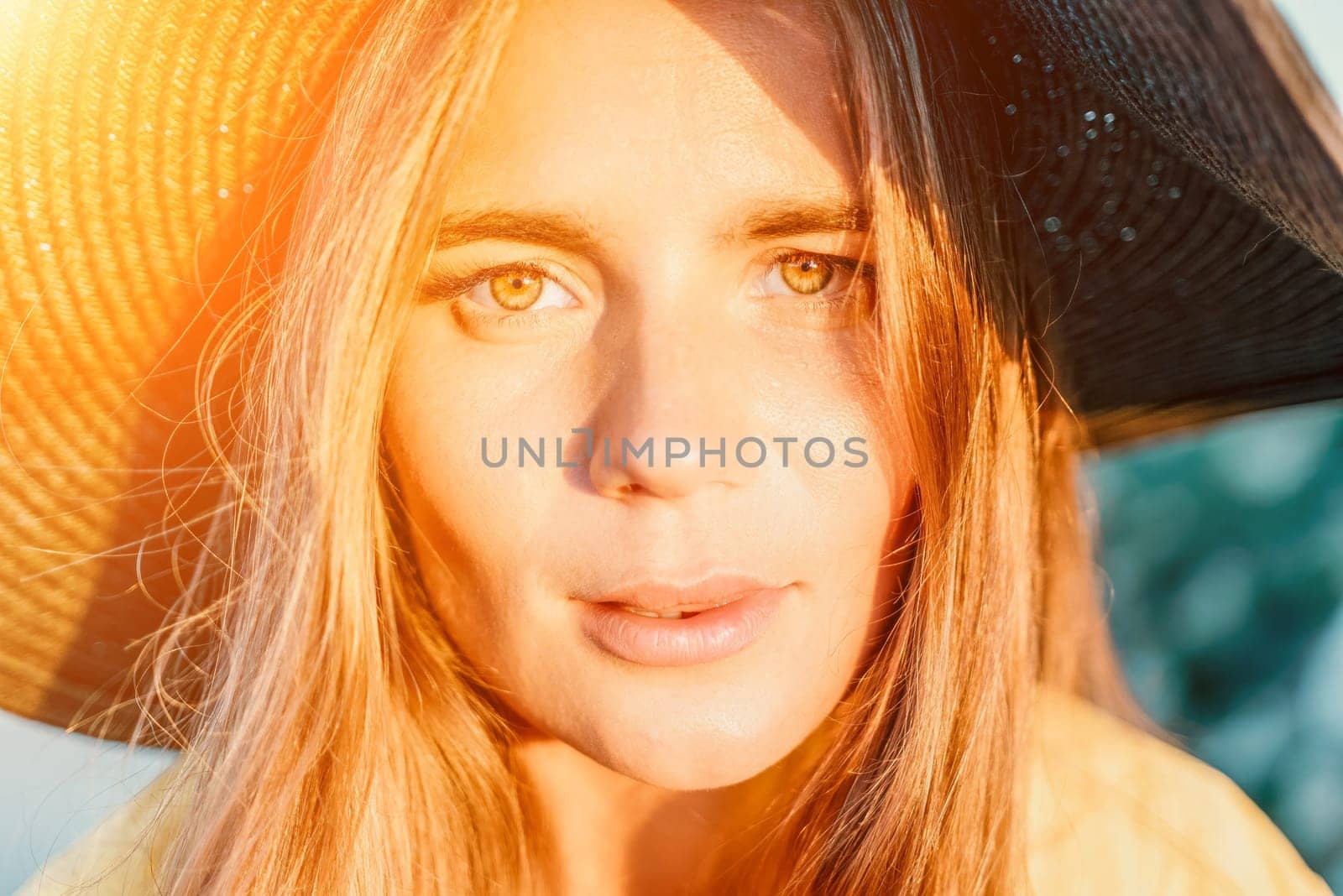 Portrait of happy young woman wearing summer black hat with large brim at beach on sunset. Closeup face of attractive girl with black straw hat. Happy young woman smiling and looking at camera at sea. by panophotograph