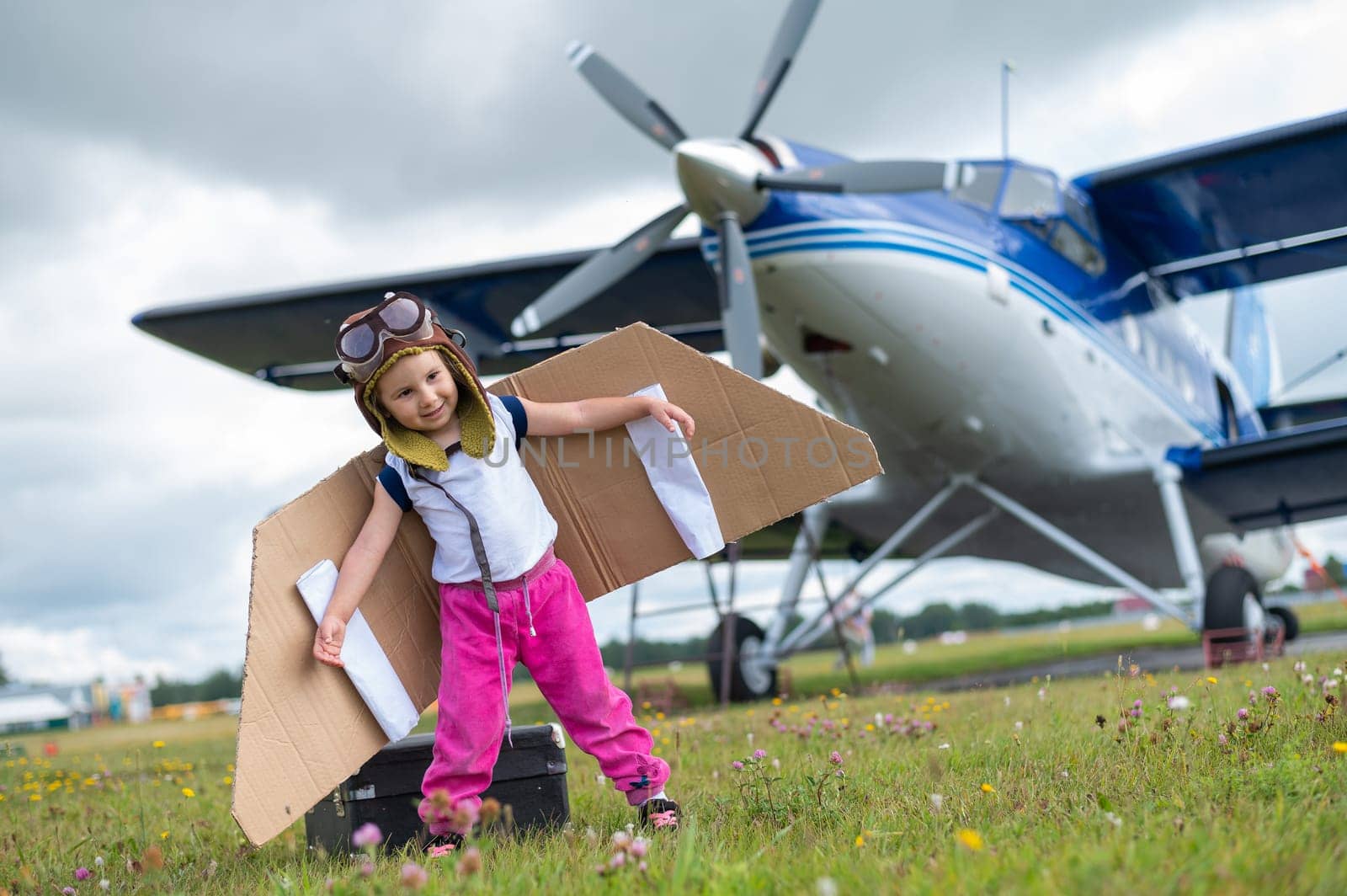 A cute little girl dressed in a cap and glasses of a pilot on the background of an airplane. The child dreams of becoming a pilot