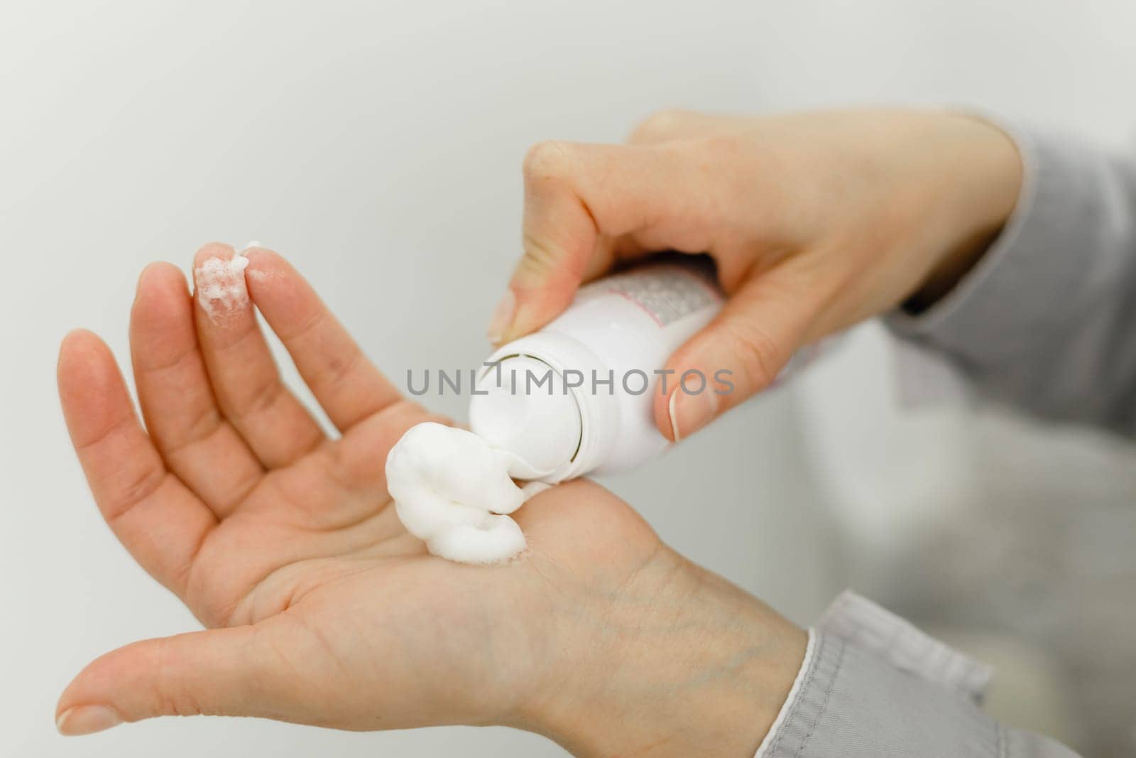 Hands of a pedicure master in a bathrobe and black gloves squeeze cream from the bottle. Close-up