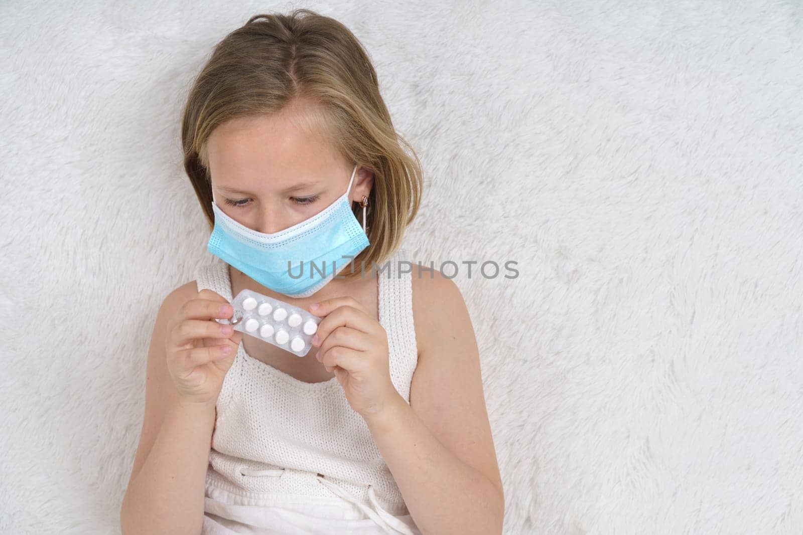 A sick teenage girl in a protective mask squeezes pills out of a package. Medical concept.