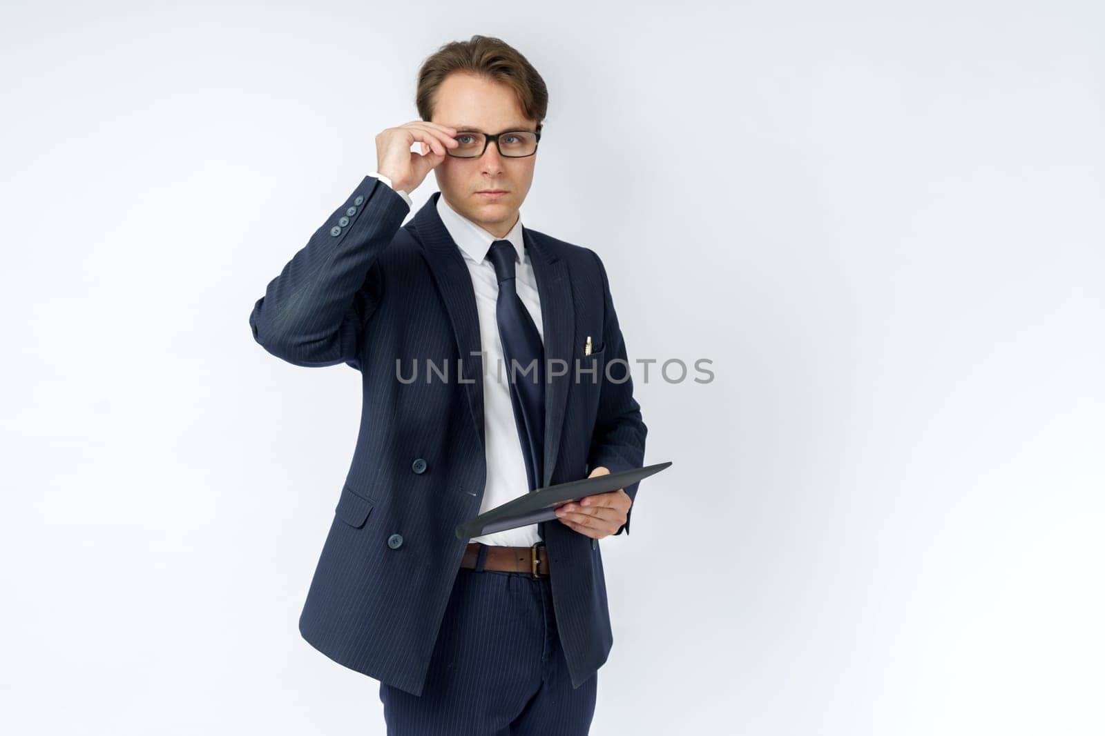 Portrait of a businessman in a blue suit who is holding an electronic tablet in his hands and adjusting his glasses. White background. Business and finance concept