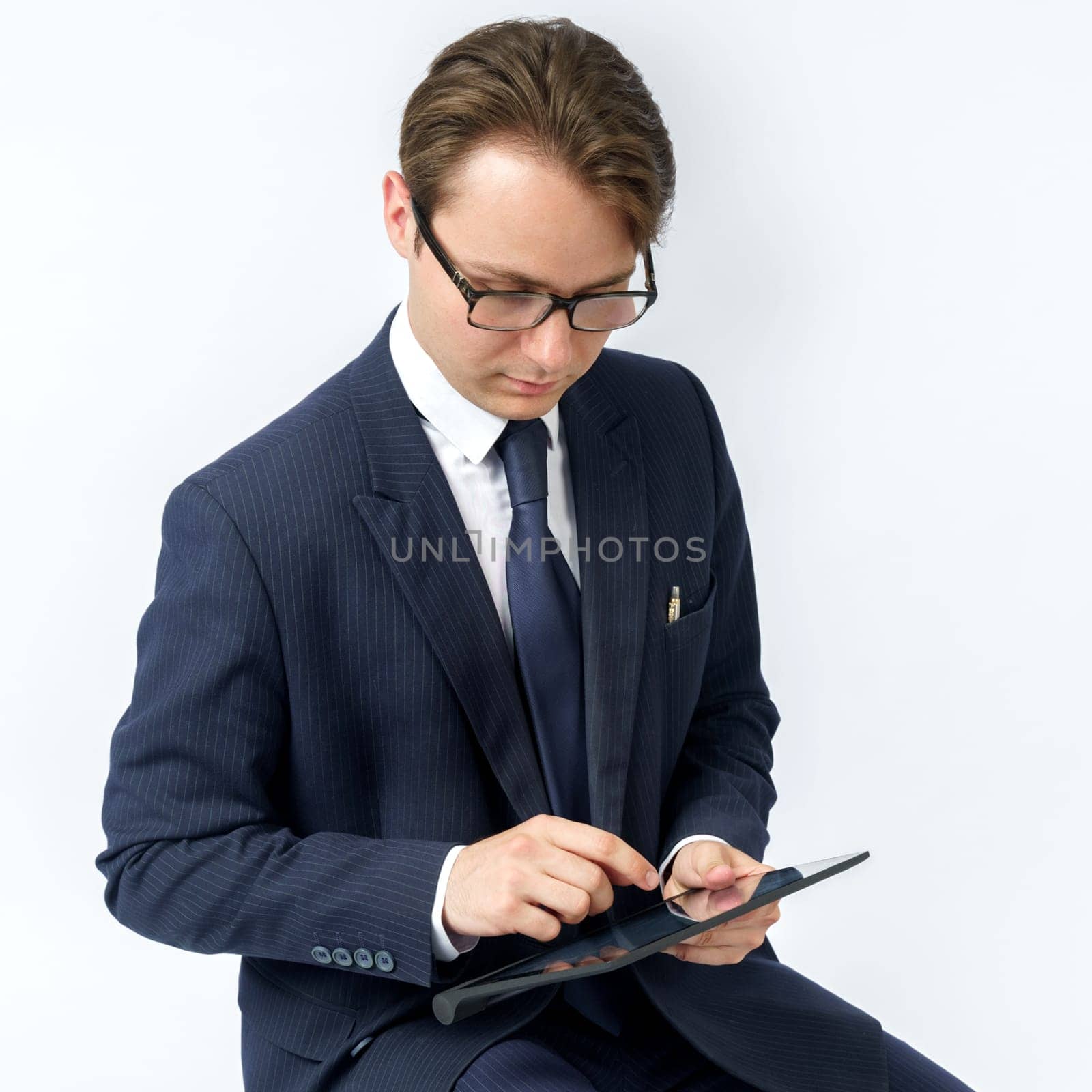 Portrait of a businessman in a blue suit who sits and works with an electronic tablet. White background. Business and finance concept