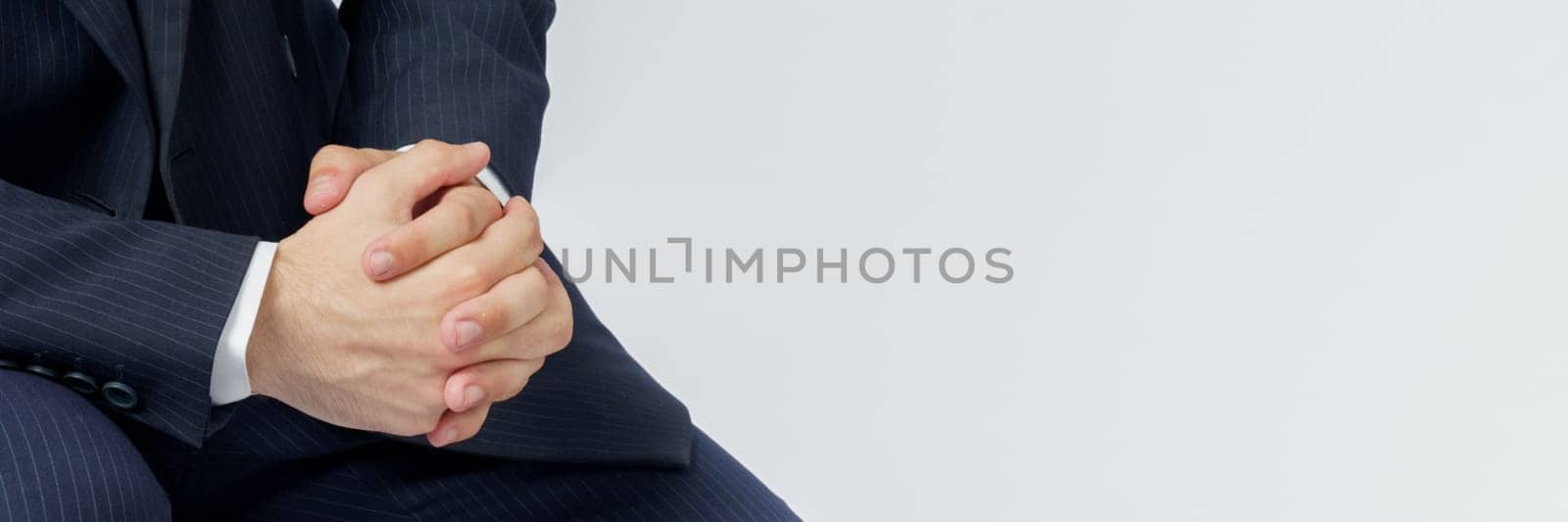 A portrait of a businessman in a blue suit who is clutching his hands. White background. No face visible. Business and finance concept
