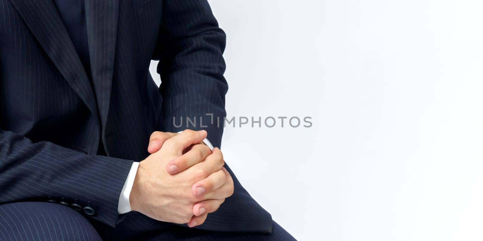 A portrait of a businessman in a blue suit who is clutching his hands. White background. No face visible. Business and finance concept