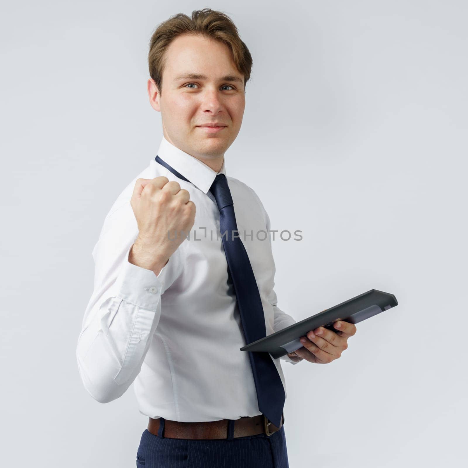 Portrait of a businessman raised his hand clenched into a fist, in the other hand an electronic tablet. White background. Business and finance concept