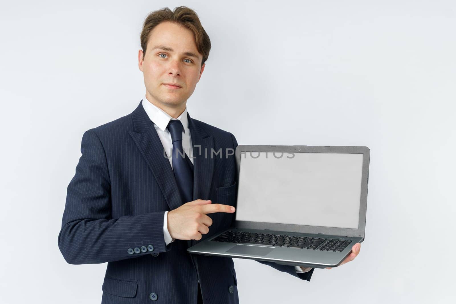 A businessman holds a laptop, the other hand shows the screen. White background. Business and finance concept