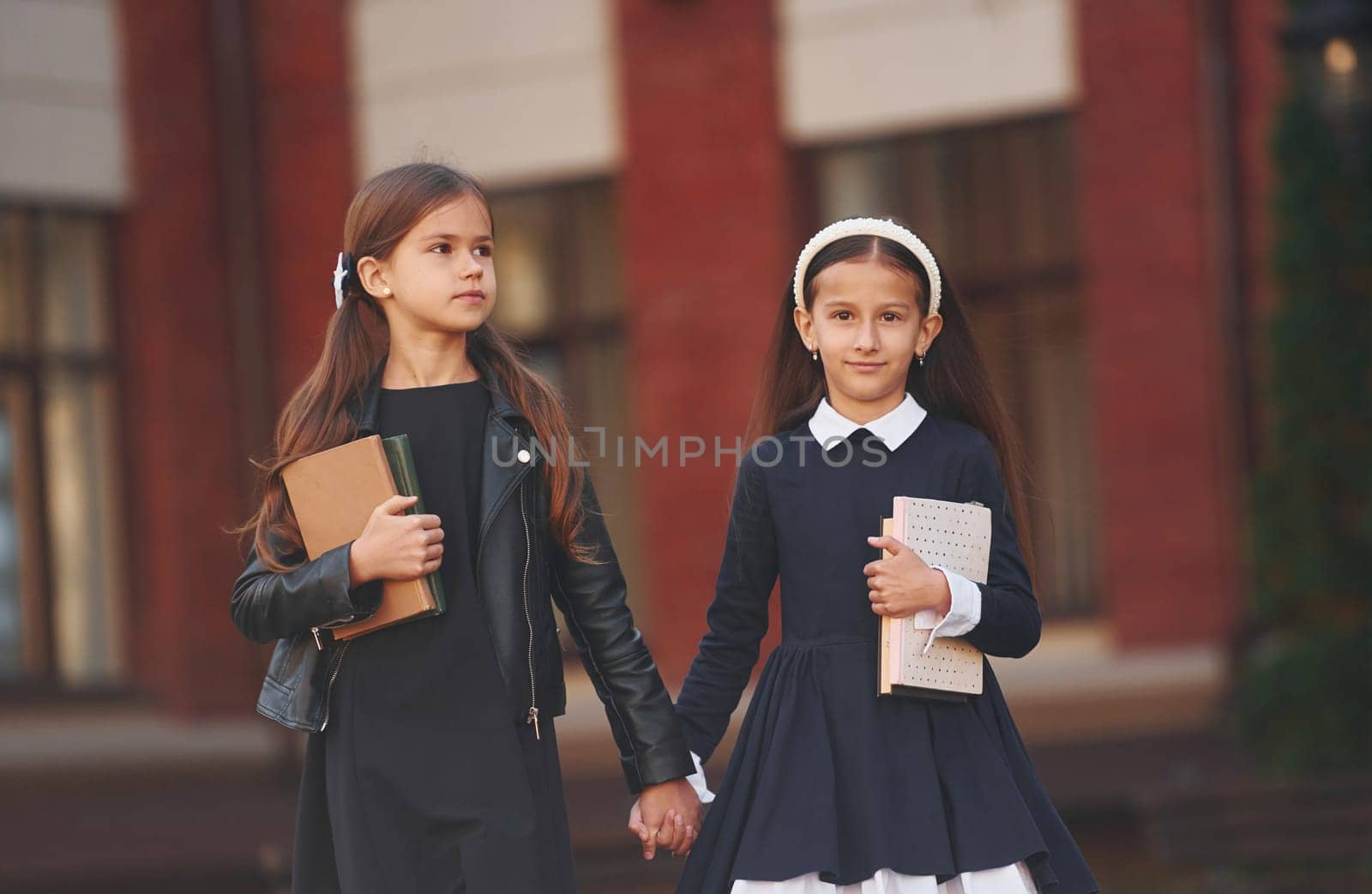 Walking together. Two schoolgirls is outside near school building.