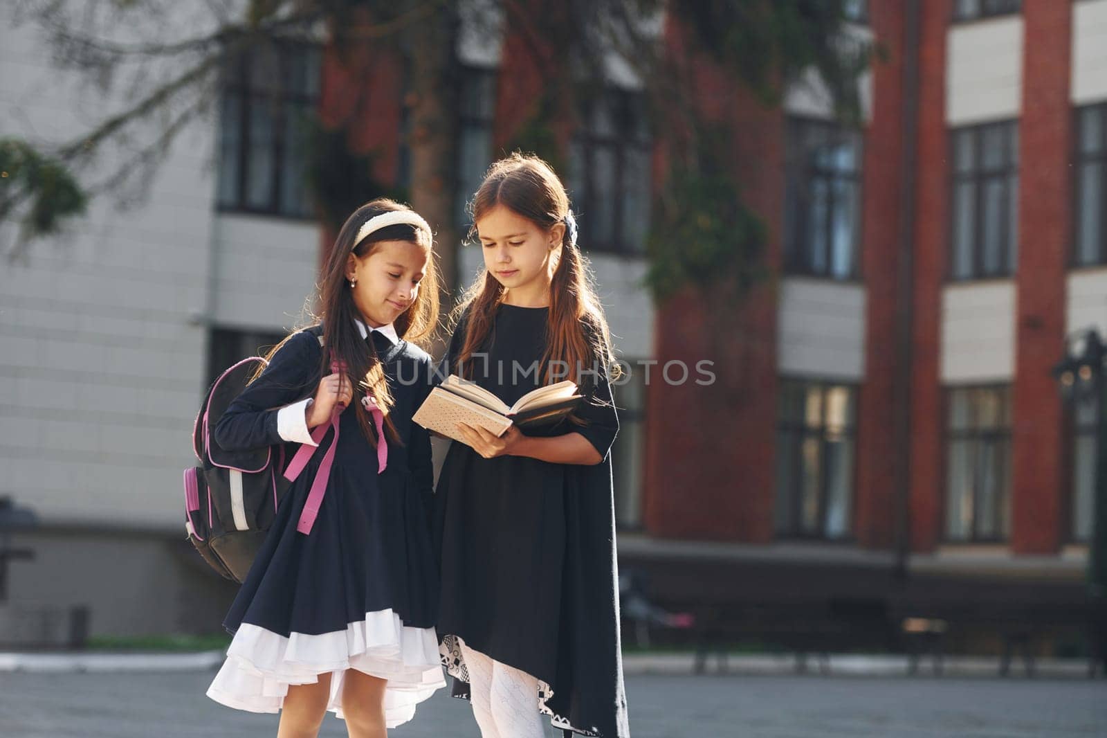 Walking together. Two schoolgirls is outside near school building.