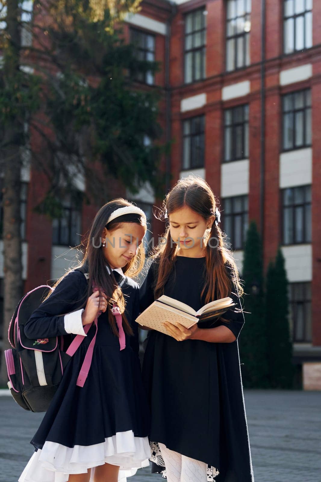 With books. Two schoolgirls is outside together near school building.