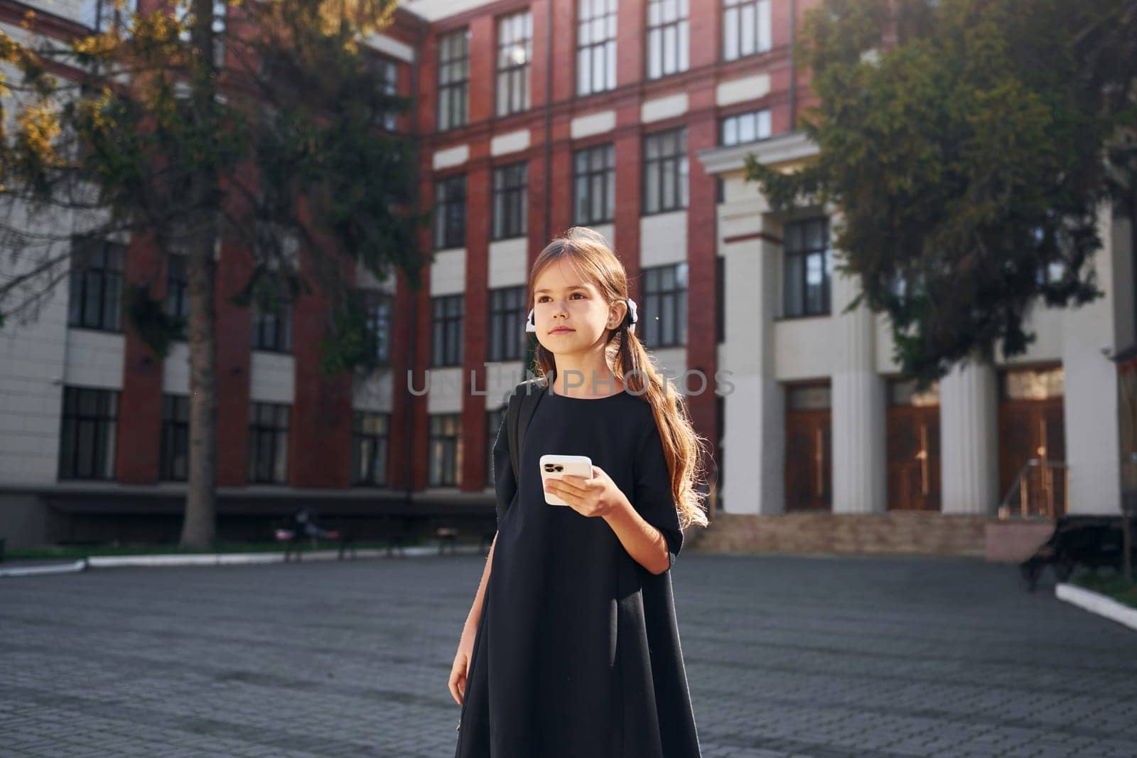 In black uniform. Schoolgirl is outside near school building.