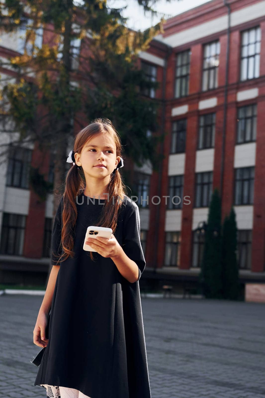 In black uniform. Schoolgirl is outside near school building.