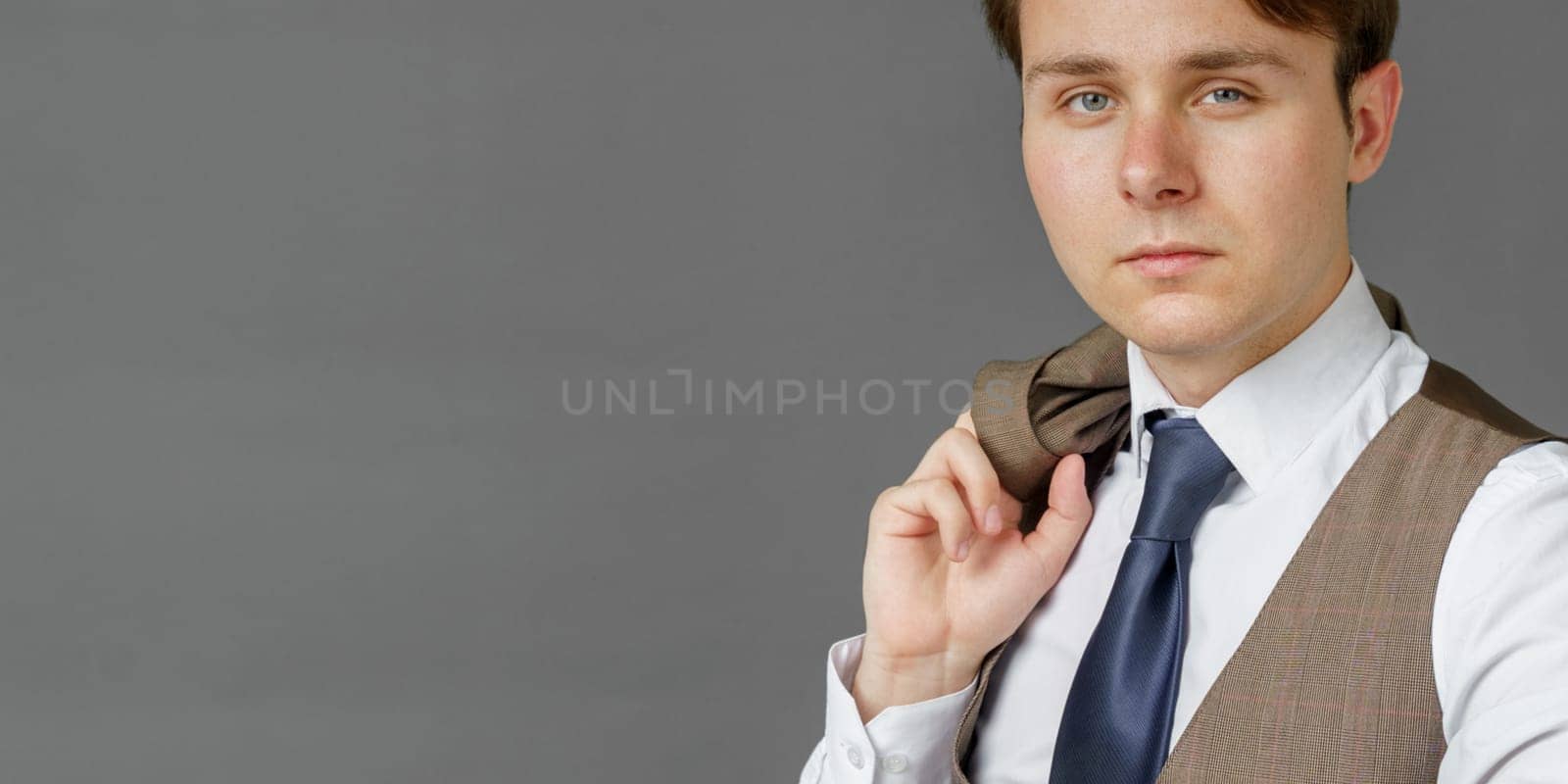 Portrait of a businessman who looks into the camera and holds a jacket over his shoulder. Gray background. Business and finance concept