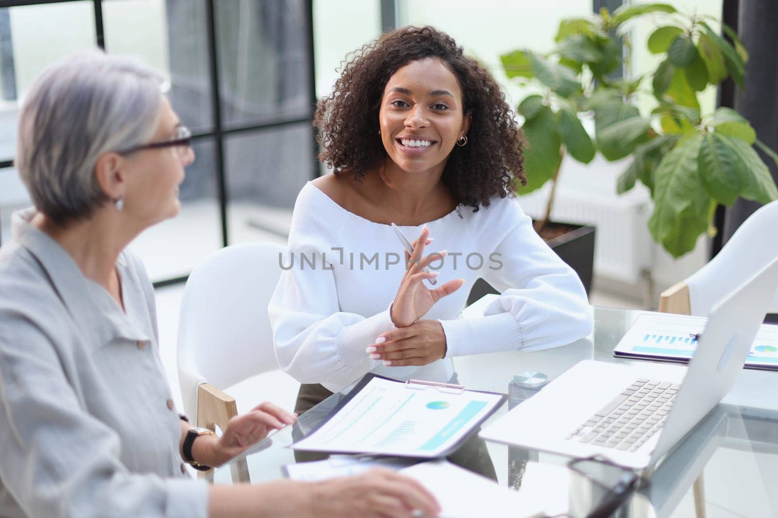 Business women smile while working together on a laptop at a table in the boardroom in the office