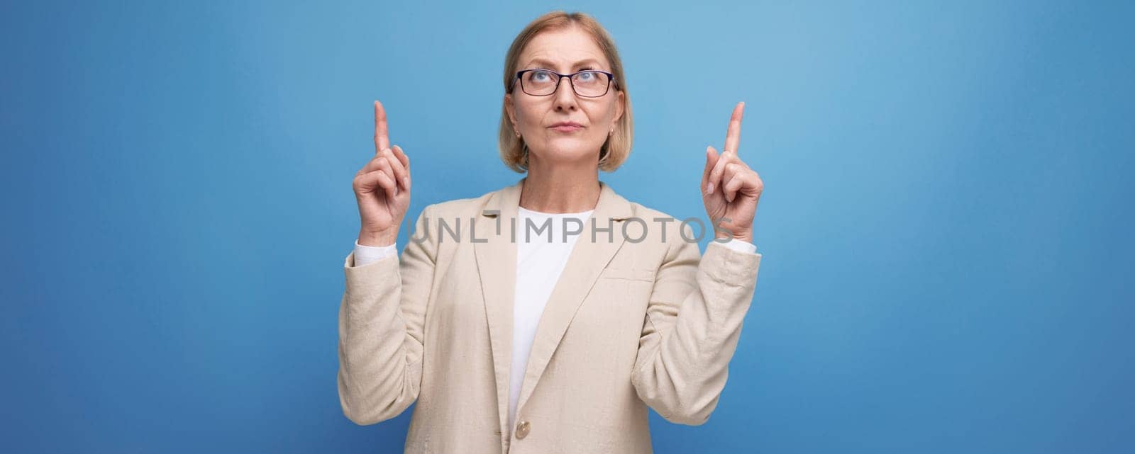 business 50s adult woman with a bob hairstyle in a fashionable jacket demonstrates space for a banner on a bright background with copy space by TRMK