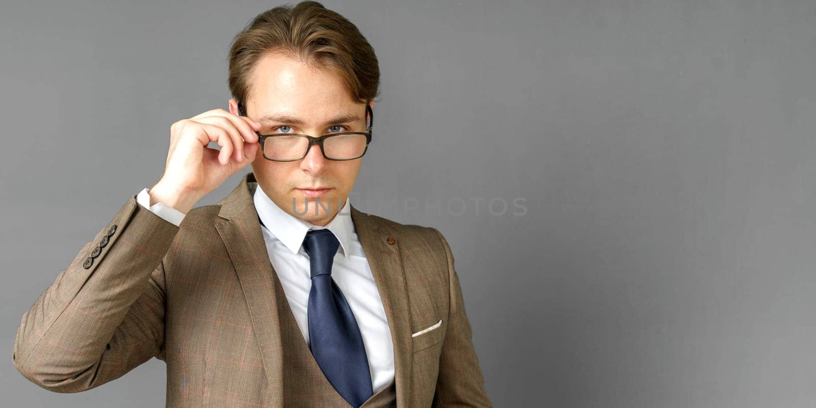 Portrait of a businessman in a suit looking at the camera and adjusting his glasses. Gray background. Business and finance concept