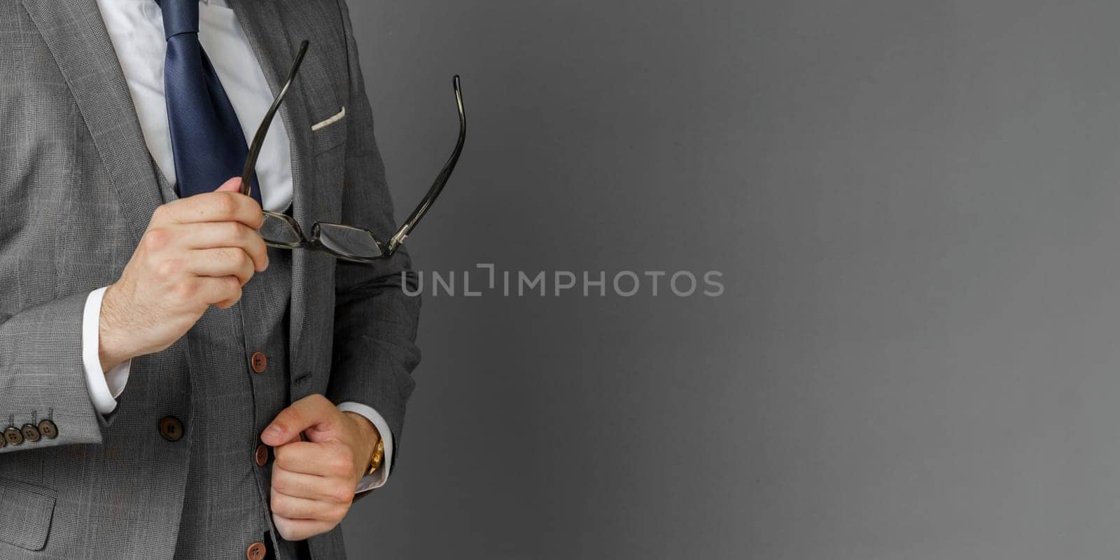 Portrait of a businessman in a suit who adjusts his glasses. The face is not visible. Gray background concept of business and finance