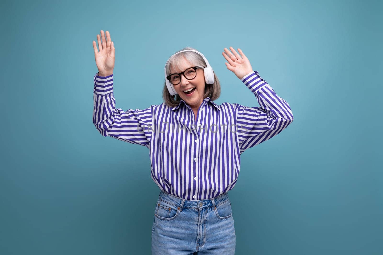 happy middle aged woman with gray hair with headphones on bright studio background.