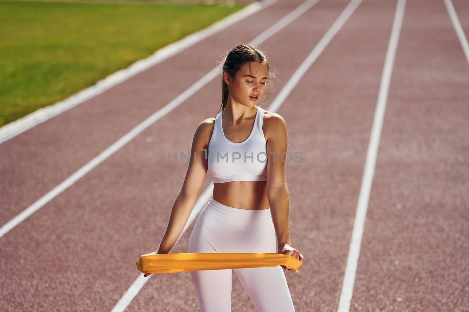Holding streching equipment. Young woman in sportive clothes is exercising outdoors.