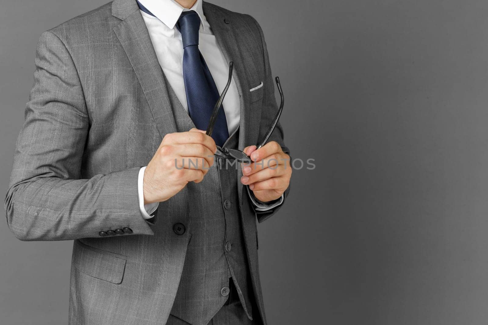 Portrait of a businessman in a suit who adjusts his glasses. The face is not visible. Gray background concept of business and finance