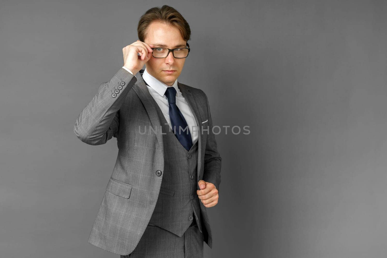 Portrait of a businessman in a suit, who adjusts his glasses. Gray background. Business and finance concept