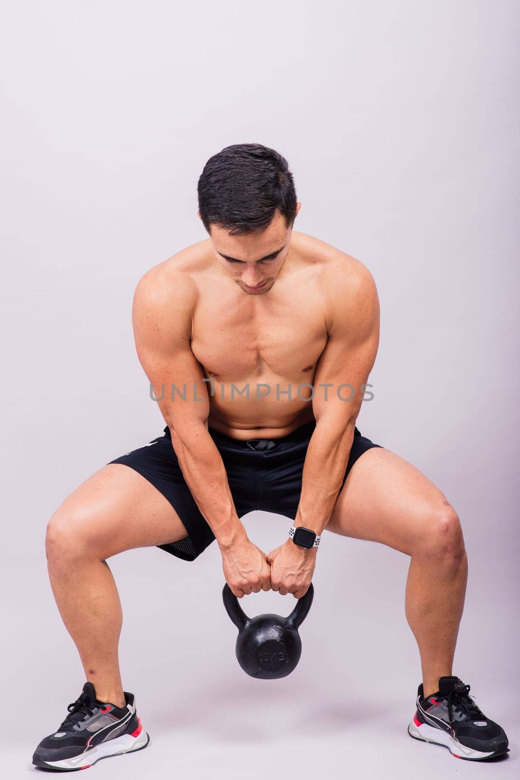 Hispanic male athlete working out with kettlebell on a grey background. Crossfit workout theme.