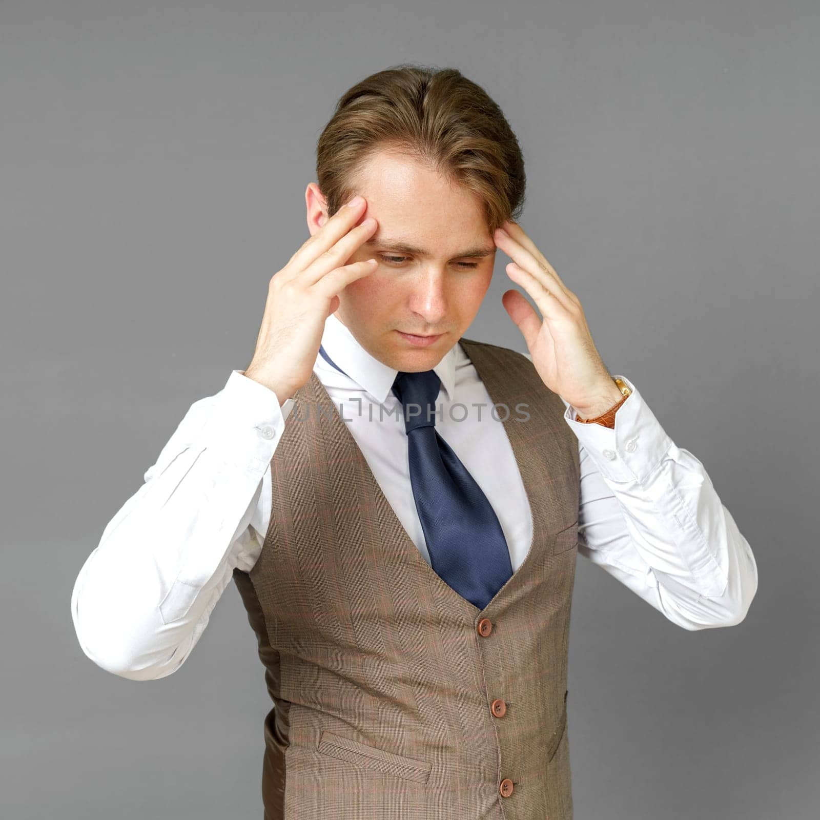 An emotional portrait of a businessman who touches his head with his hands. Gray background. Business and finance concept