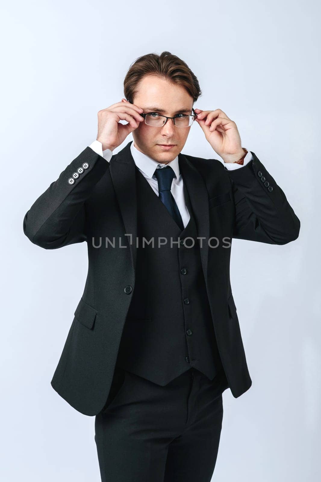Business and finance concept. A man in a black suit adjusts his glasses. Light background