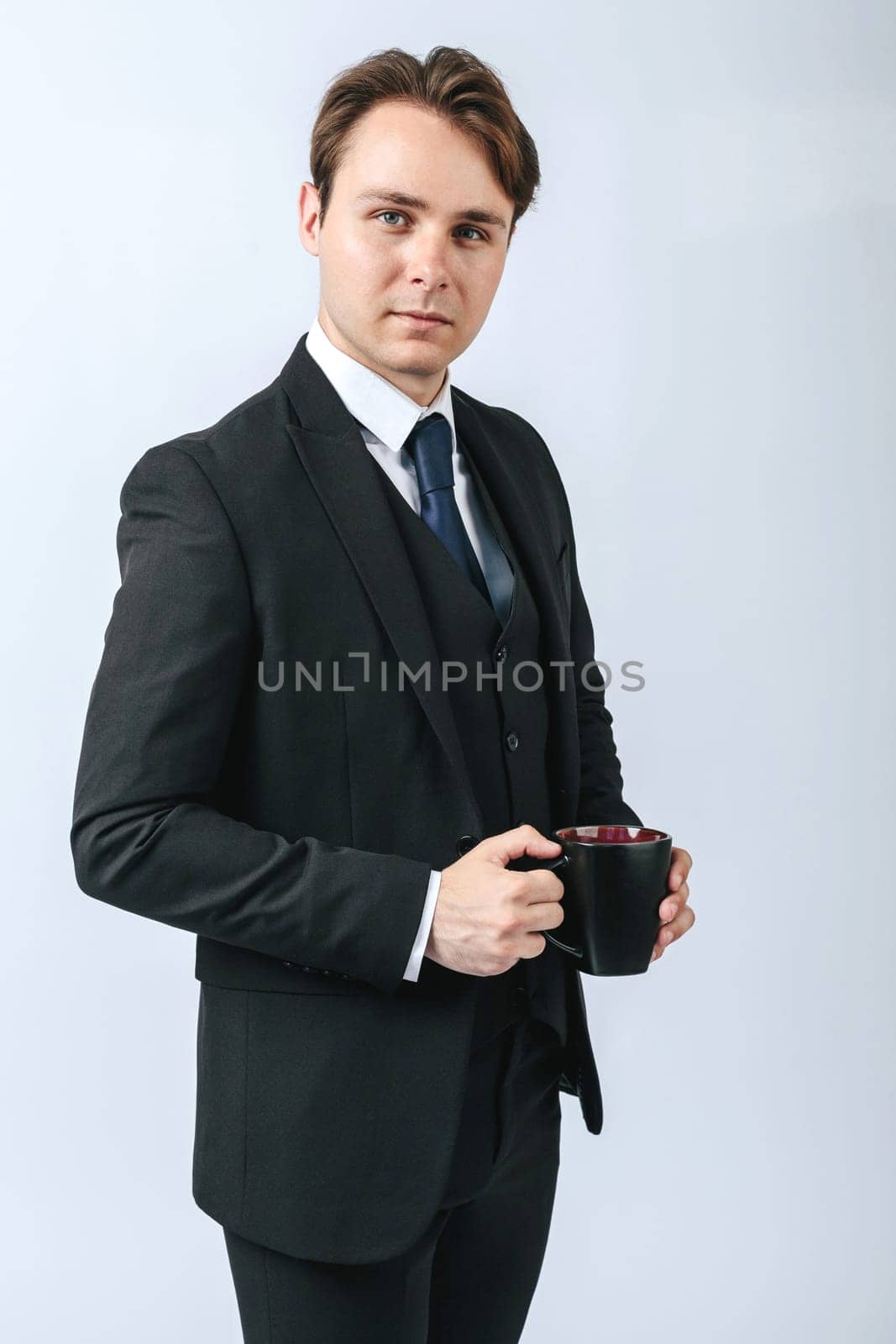 Business and finance concept. A man in a black suit holds a cup of coffee in his hands. Light background
