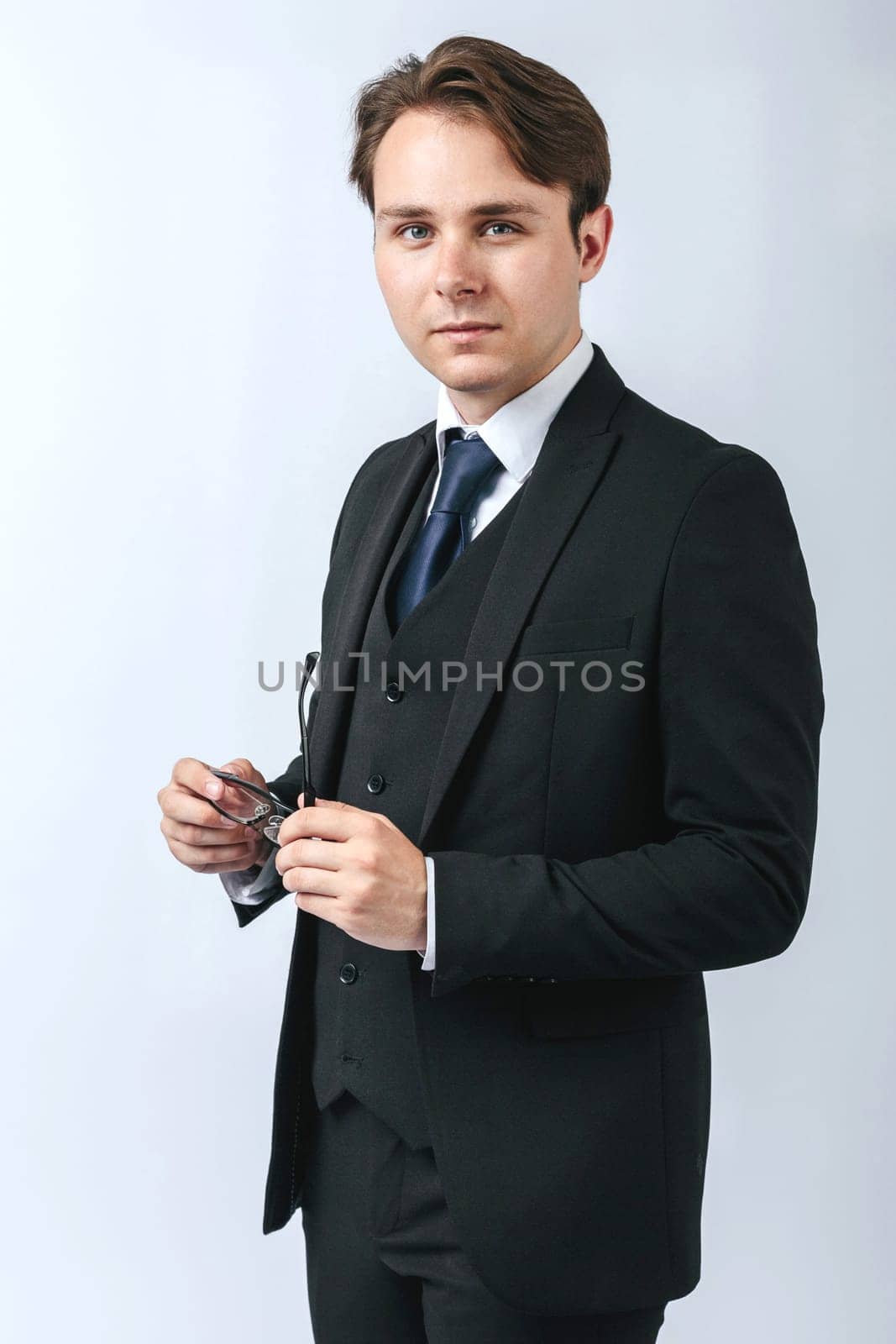 Business and finance concept. A man in a black suit holds glasses in his hands. Light background