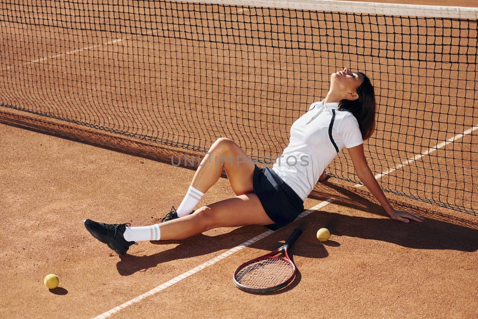 Sitting near the net. Female tennis player is on the court at daytime.