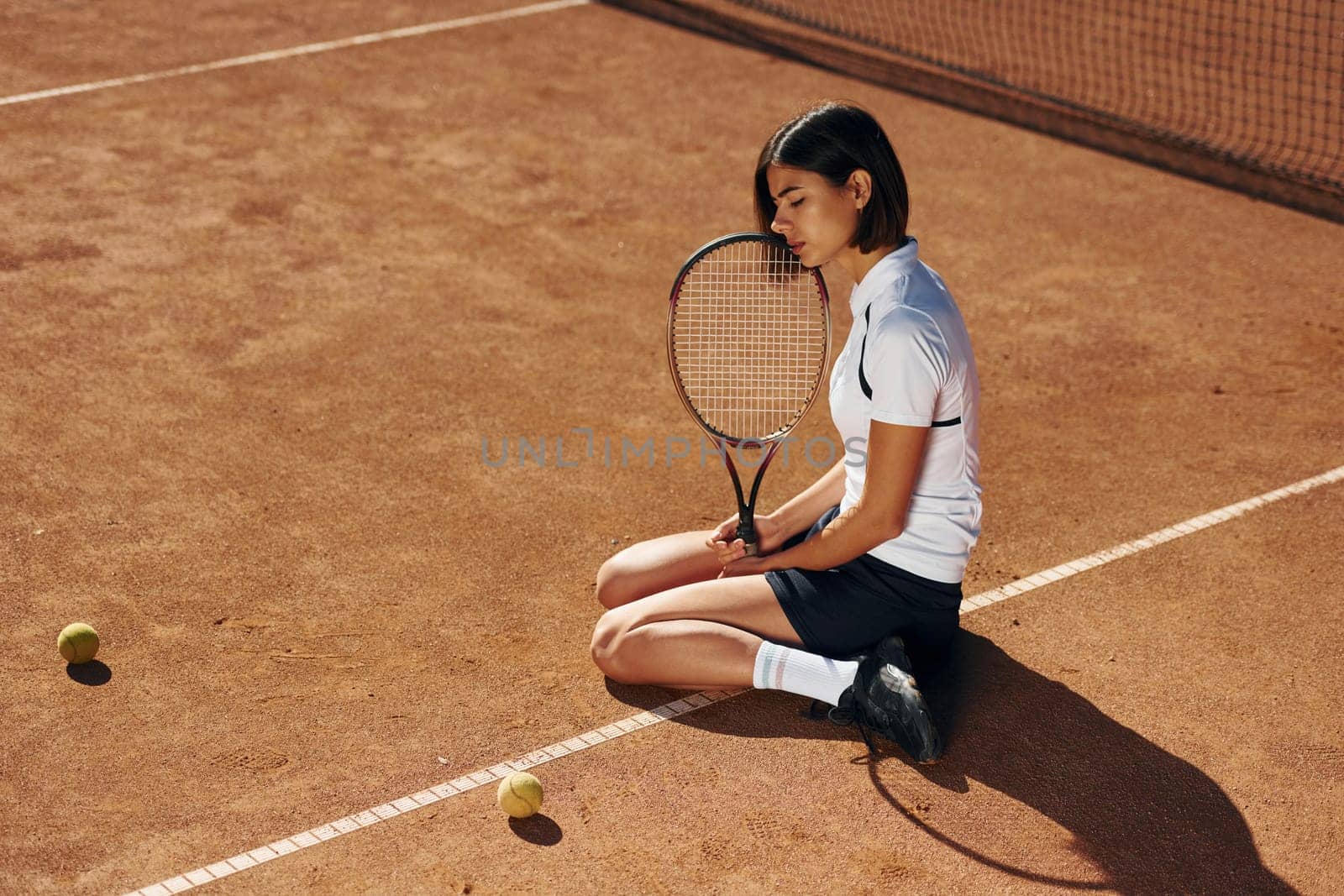 On the ground. Female tennis player is on the court at daytime.