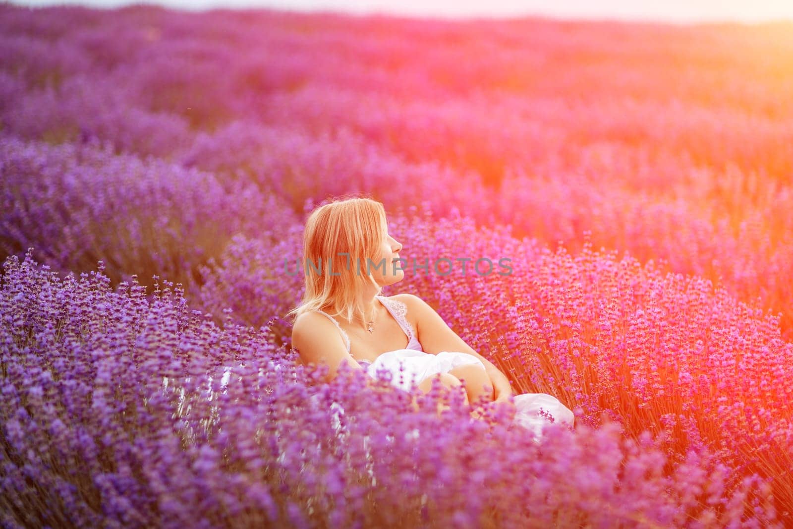 A middle-aged woman sits in a lavender field and enjoys aromathe by Matiunina