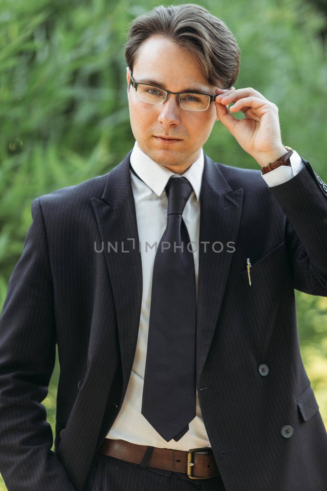 Business and finance concept. Portrait of a businessman adjusting his glasses. In the park