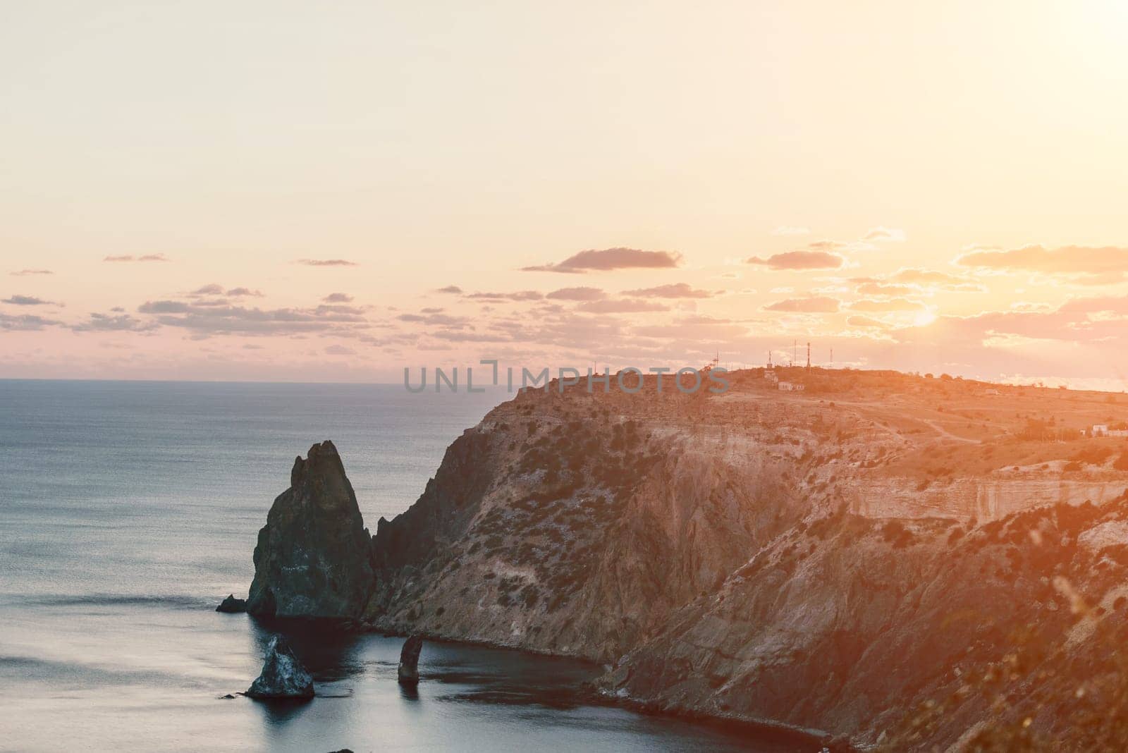 A red burning sunset with the silhouette of a cliff over the sea. Abstract nature summer or spring ocean sea background. Small waves on golden warm water surface with bokeh lights from sun.