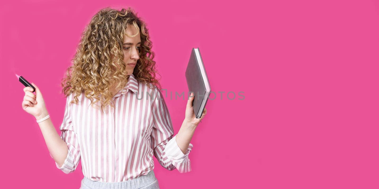 Fashionable woman in a striped shirt holding a diary and a marker. Isolated on pink background