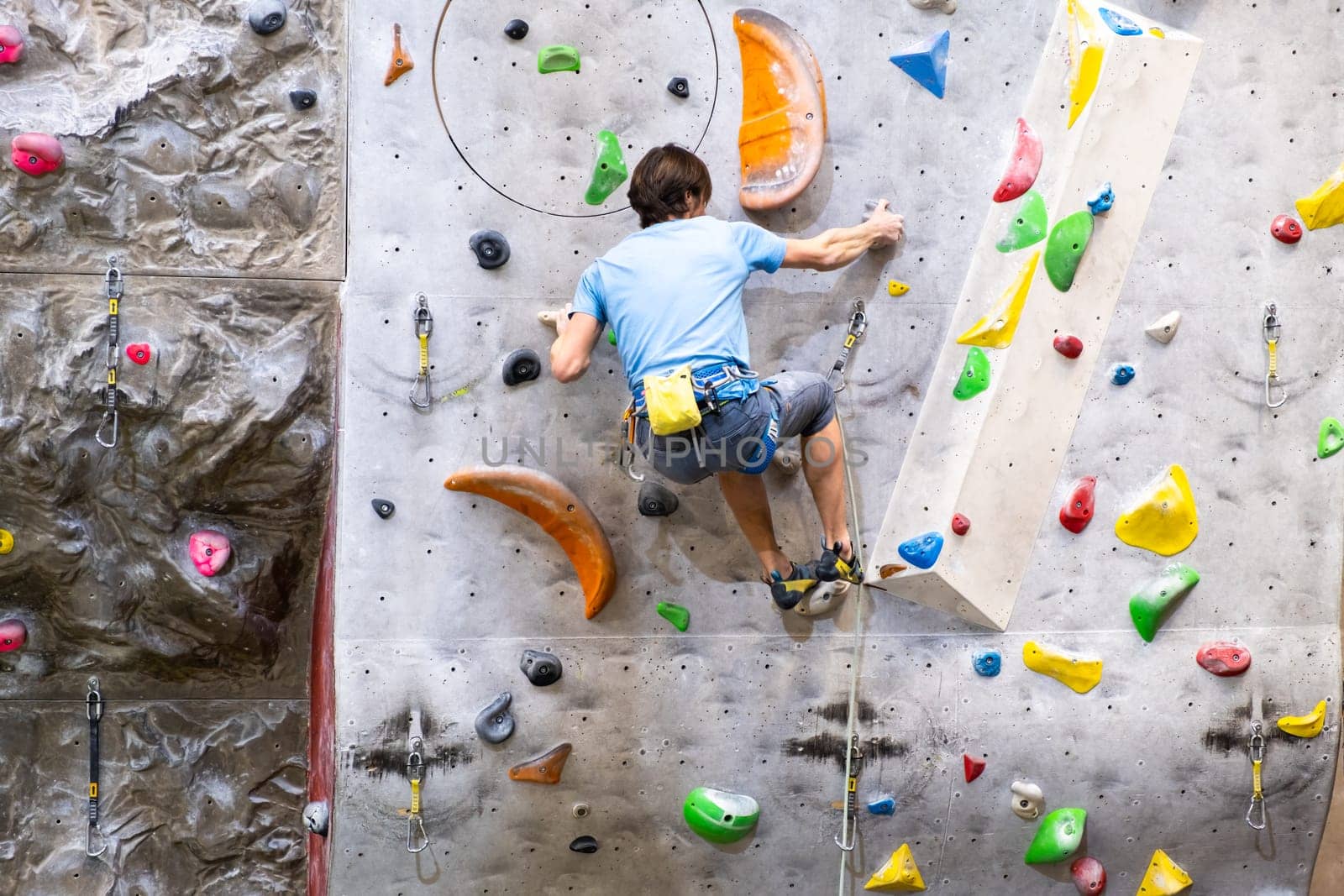 The climber trains on the artificial rock wall with insurance in bouldering gym, April 2022, Prague, Czech Republic.