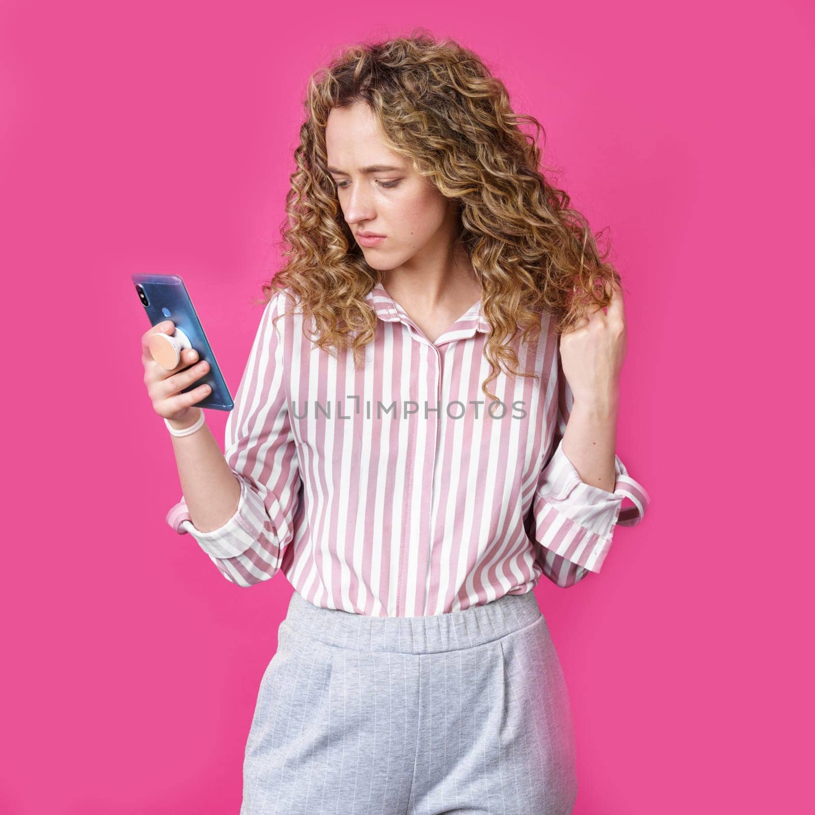 Fashionable woman in a striped shirt, reads a message on the phone. Isolated on pink background