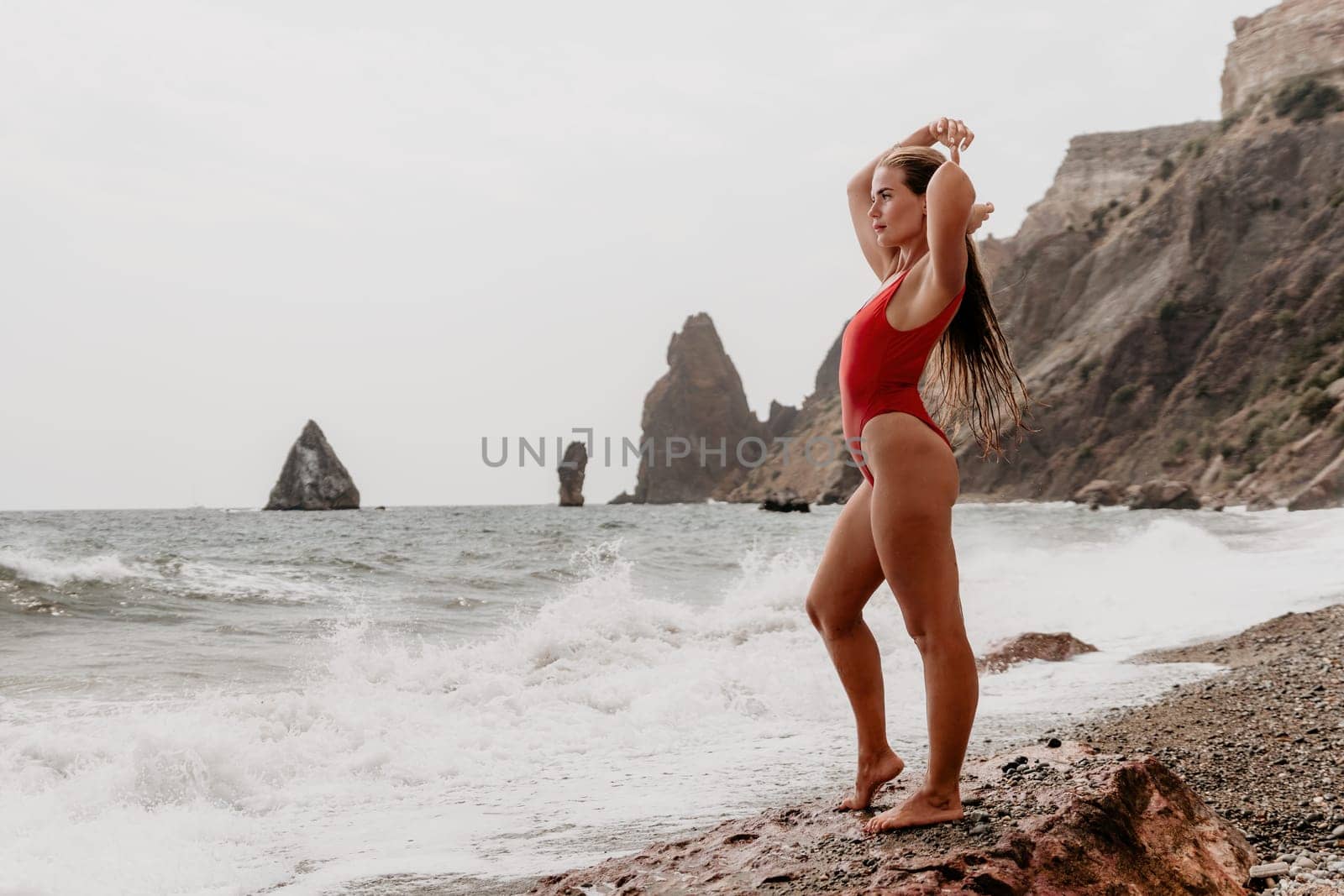 Woman summer travel sea. Happy tourist in red bikini enjoy taking picture outdoors for memories. Woman traveler posing on beach at sea surrounded by volcanic mountains, sharing travel adventure joy by panophotograph