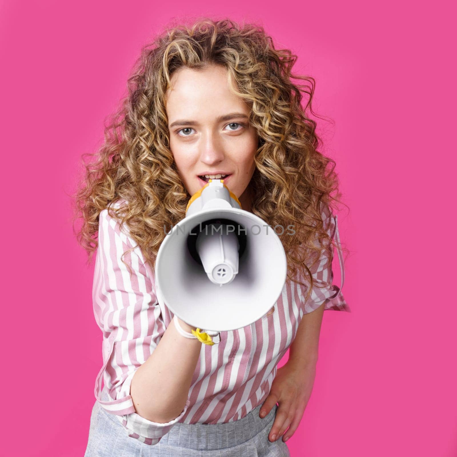 Young woman speaks into a megaphone. Isolated pink background. People sincere emotions lifestyle concept.