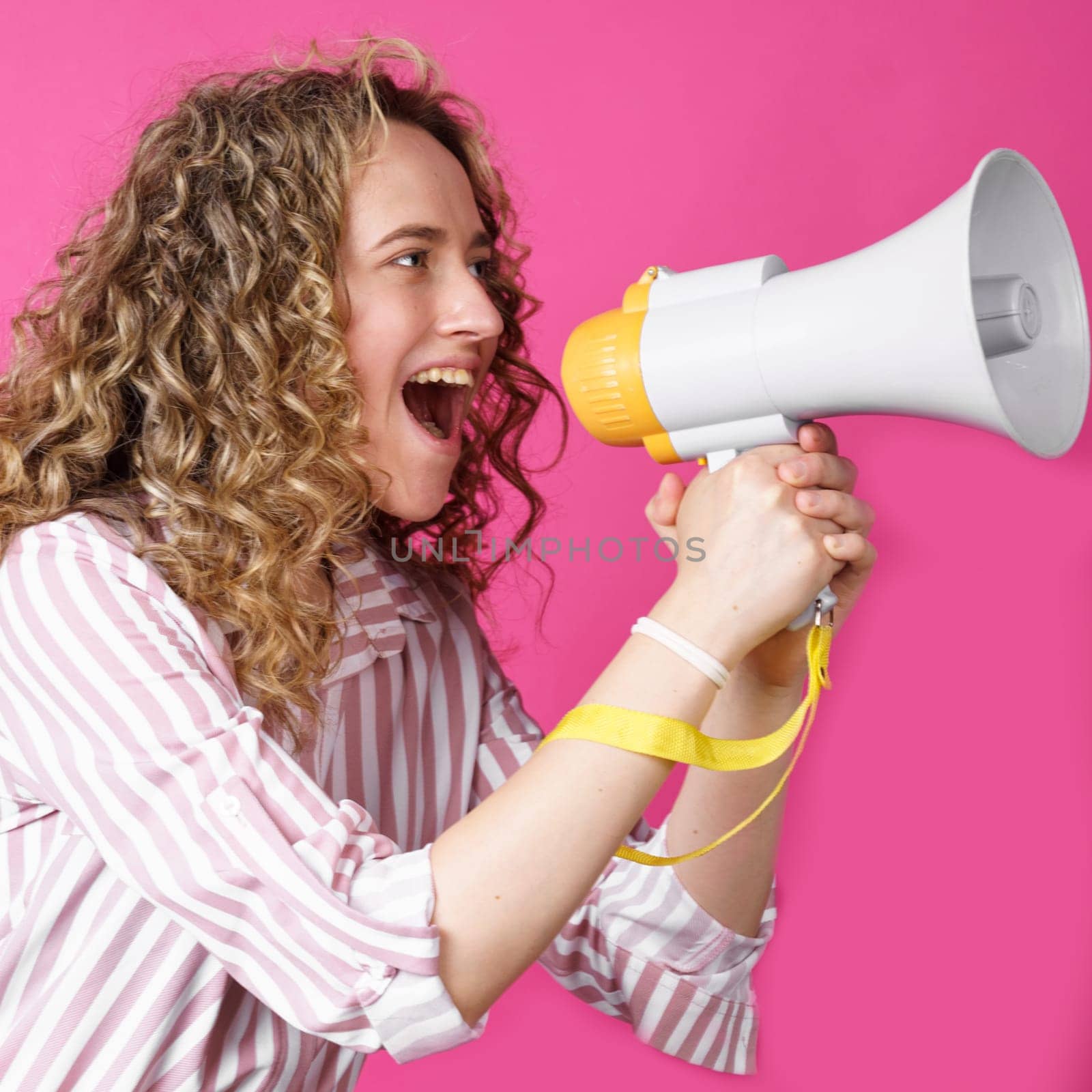 Young woman shouts into a megaphone. Isolated pink background. People sincere emotions lifestyle concept.